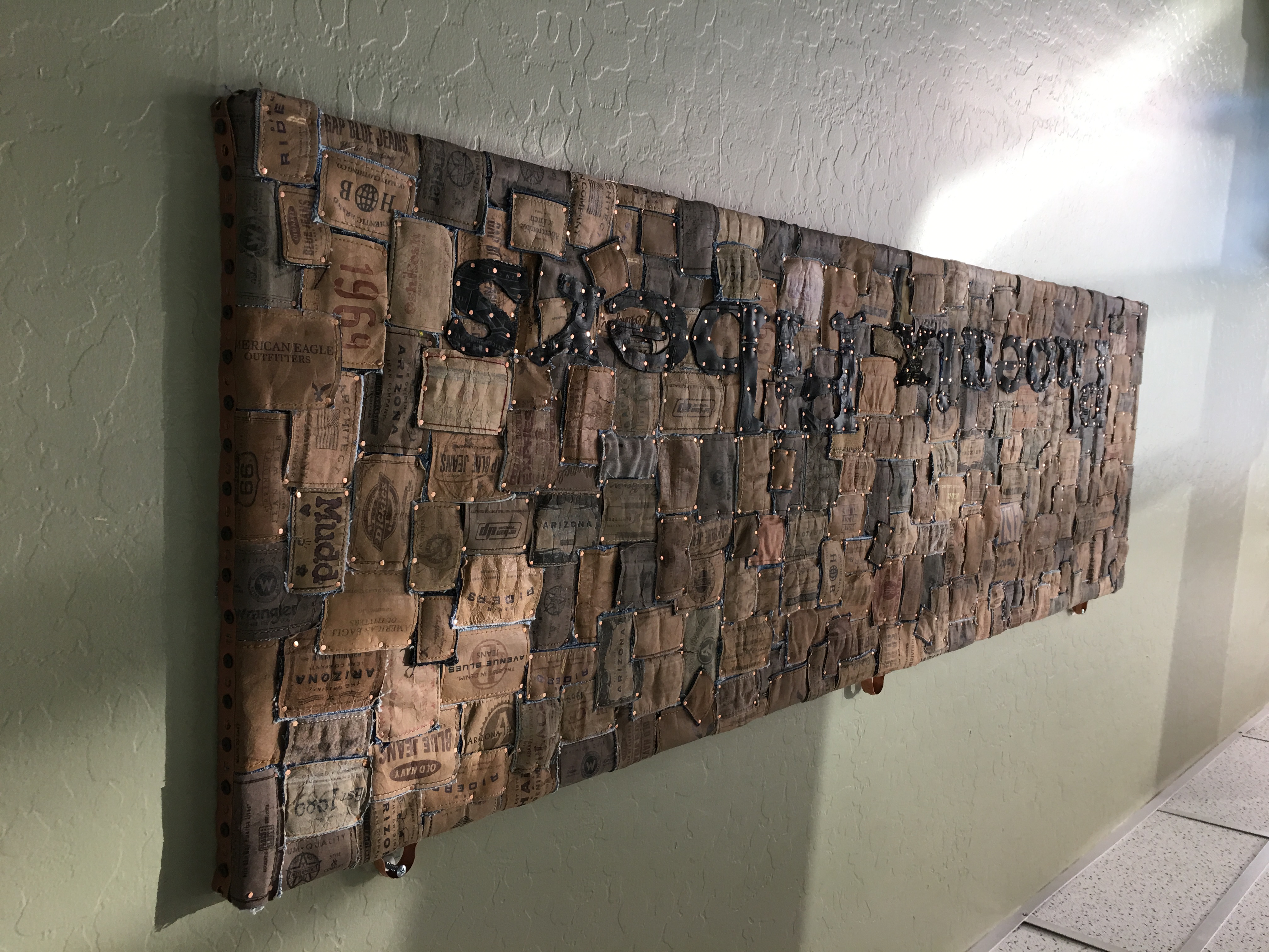 Mixed-media wall piece made of denim labels and copper rivets spelling Phoenix Riders
